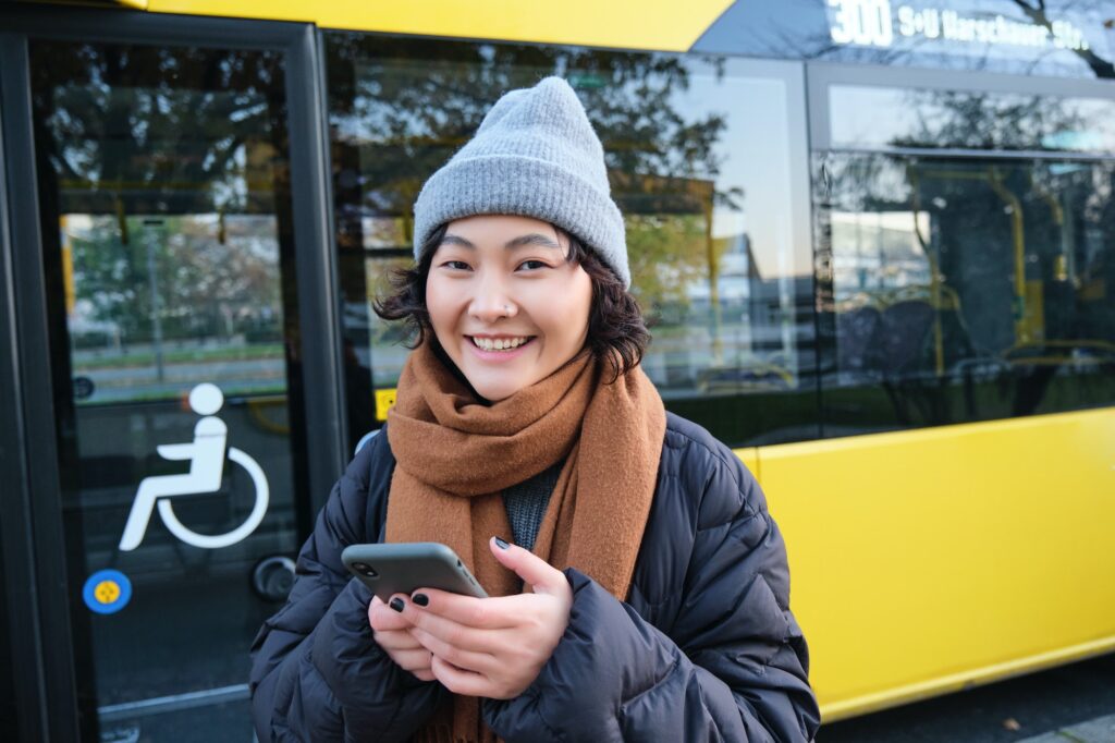 Image of girl student waiting for public transport, checks schedule on smartphone app, stands near